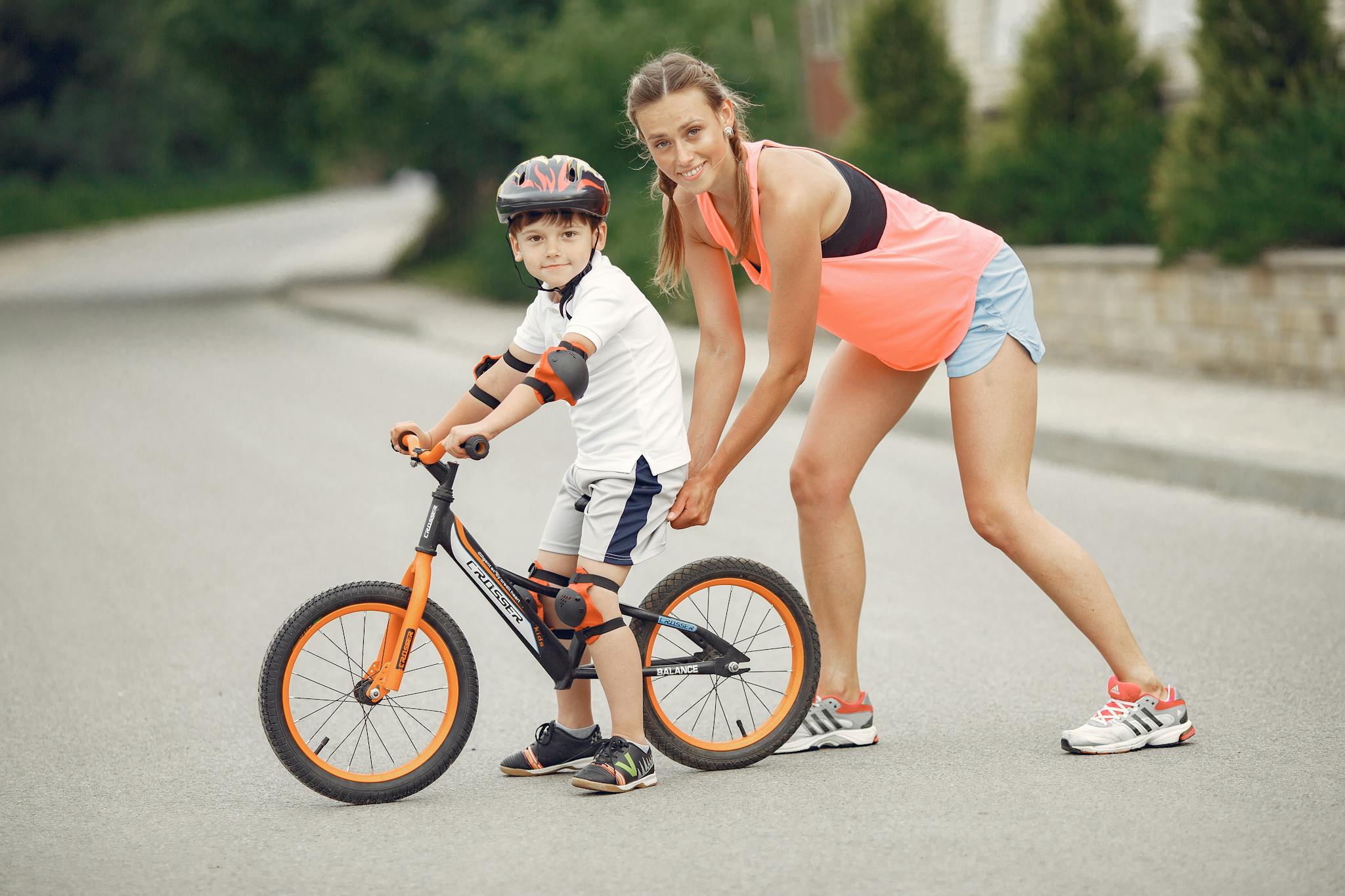 Mother helping her son ride a bicycle in a sunny outdoor setting. Bonding and learning experience.
